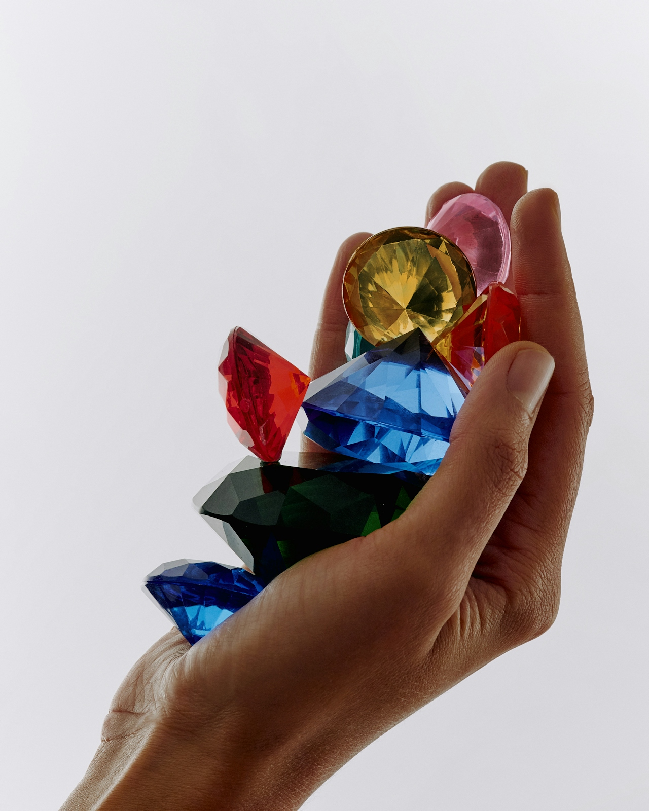 A hand cupping a small pile of cut gemstones in red, blue, yellow, green, pink.