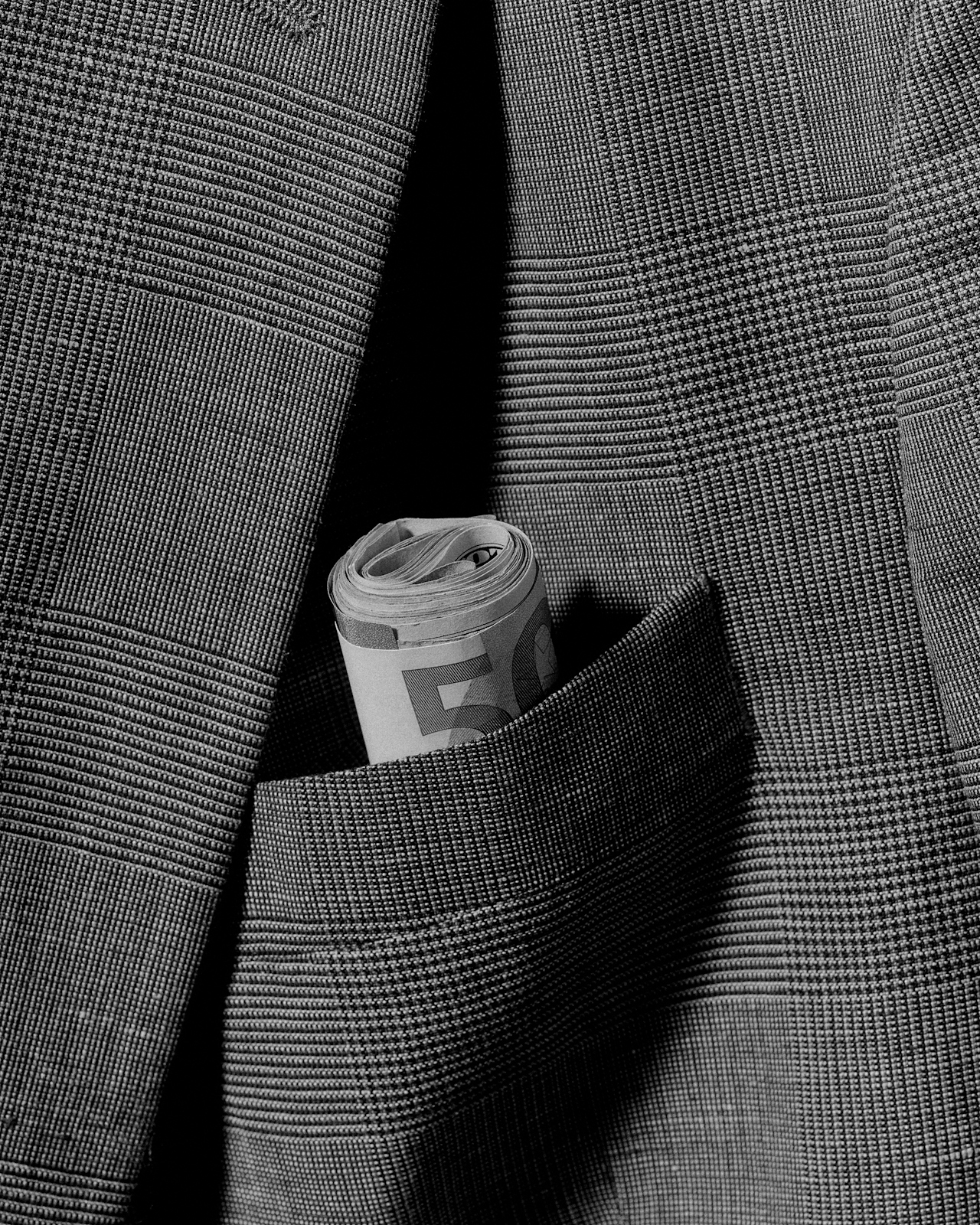 A roll of folded euro notes tucked into the breast pocket of a glen-check suit.
