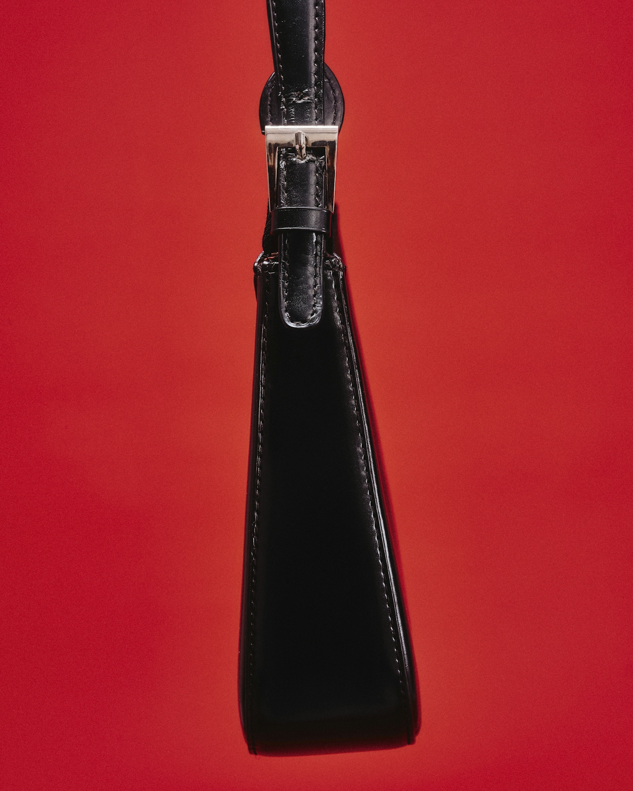 A black leather watch strap with a polished silver buckle against a deep red ground.